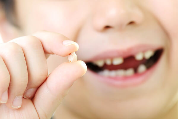 Child holding a lost baby tooth between their fingers